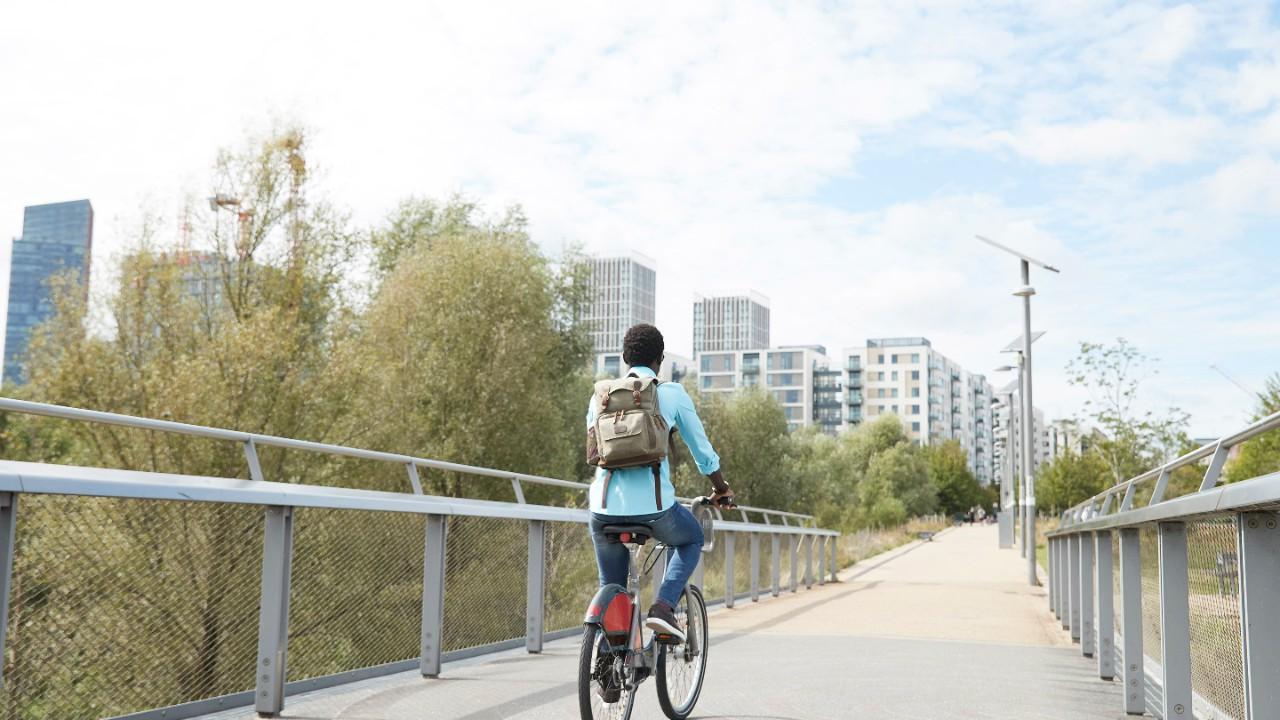 Wanita muda mengendarai sepeda melintasi jembatan menuju kota.